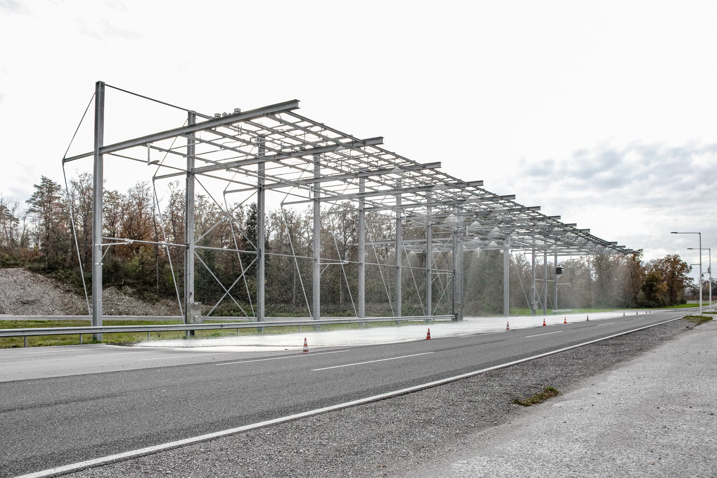 Große Stahlkonstruktion über einer Teststrecke, welche Wasser auf die Fahrbahn sprüht.