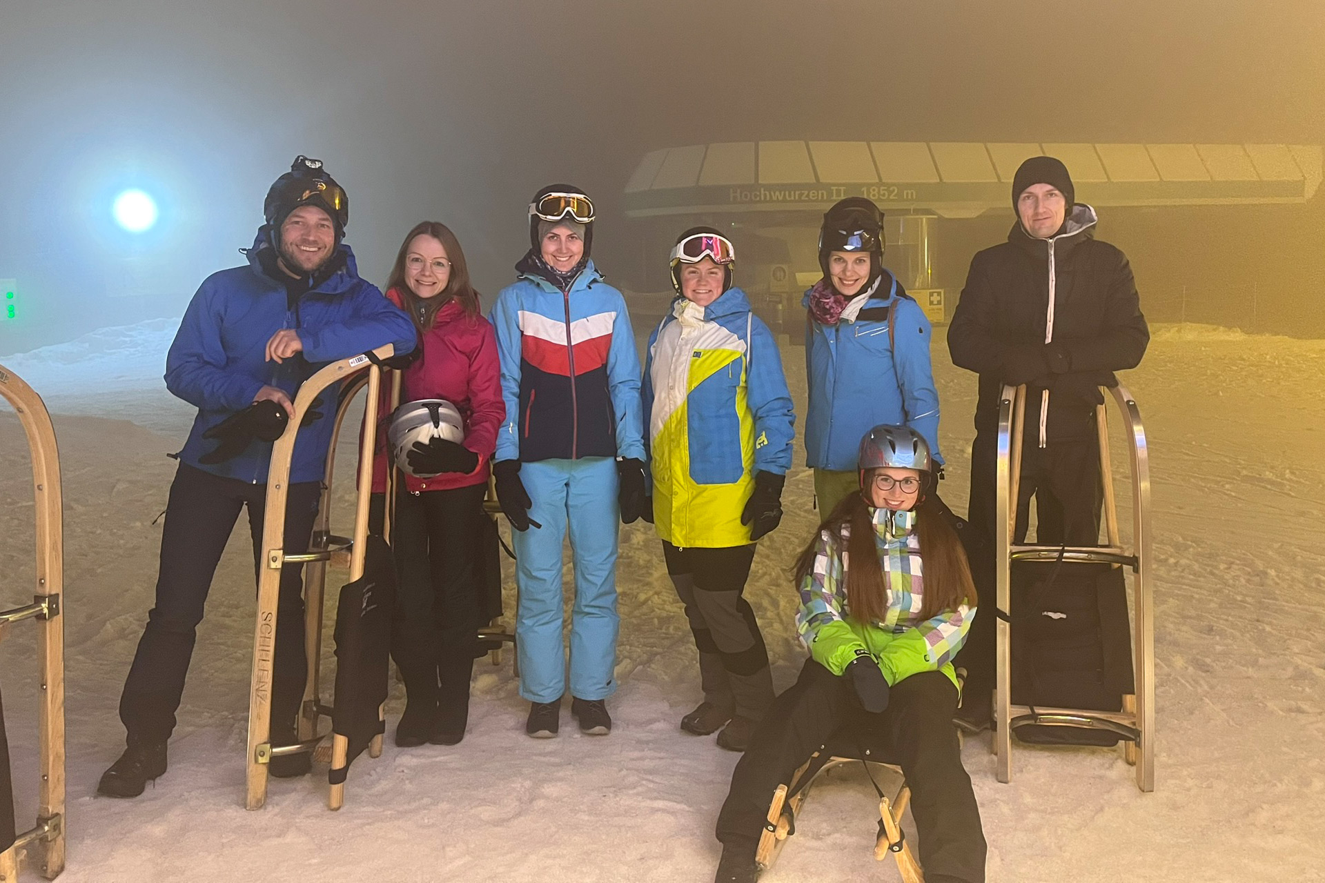 Das Digitrans-Team während eines Firmenausfluges zum Nachtrodeln auf der Hochwurzen, gekleidet in Winterausrüstung und versammelt auf einer verschneiten Piste mit Schlitten und Helmen. Digitrans team during a Firmenausflug night sledding adventure at Hochwurzen.